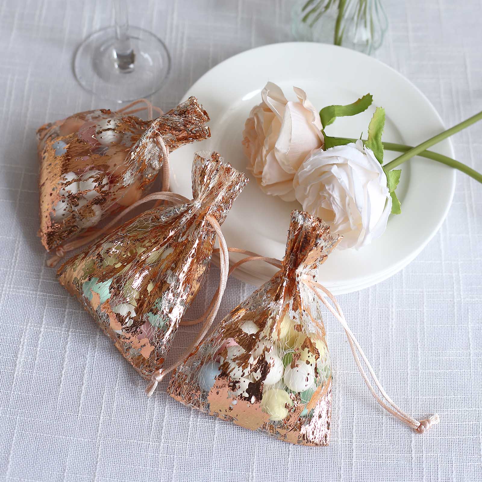 Metallic rose gold drawstring candy bags on a plate with flowers.