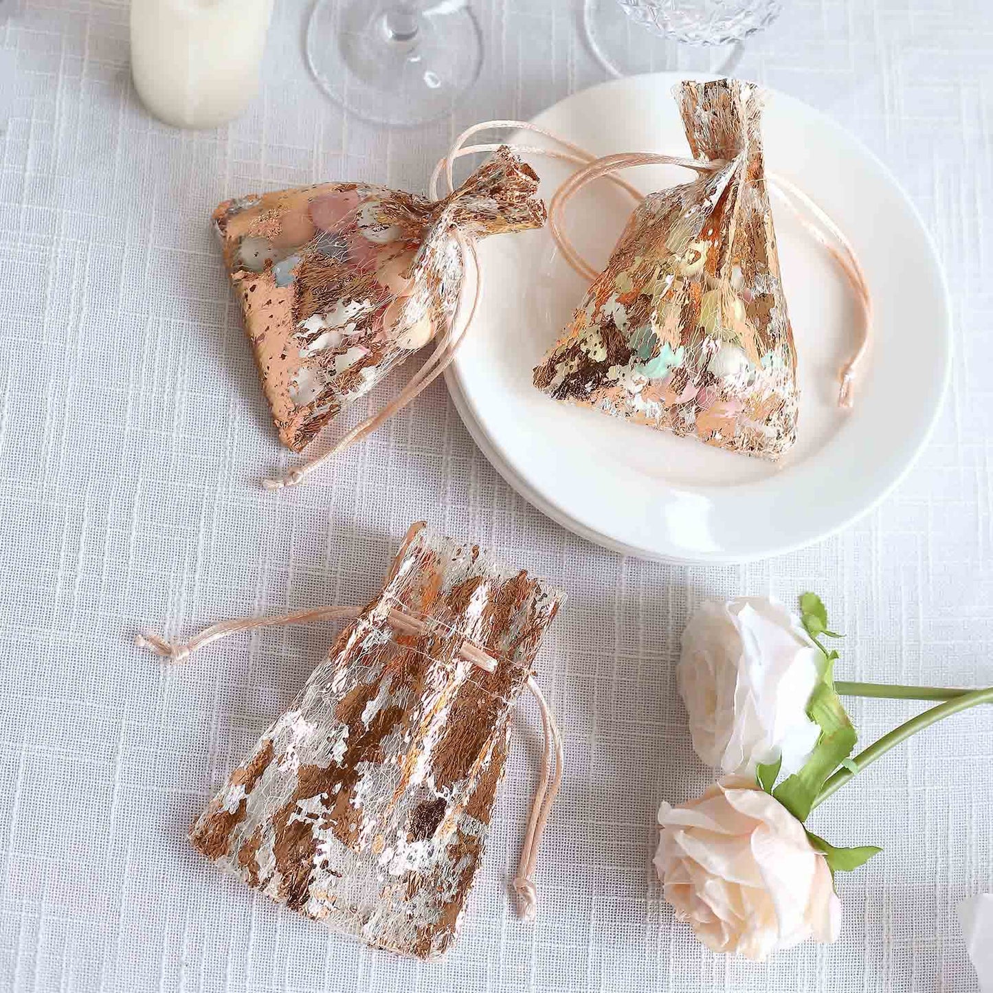 Metallic rose gold drawstring candy bags on a table setting.
