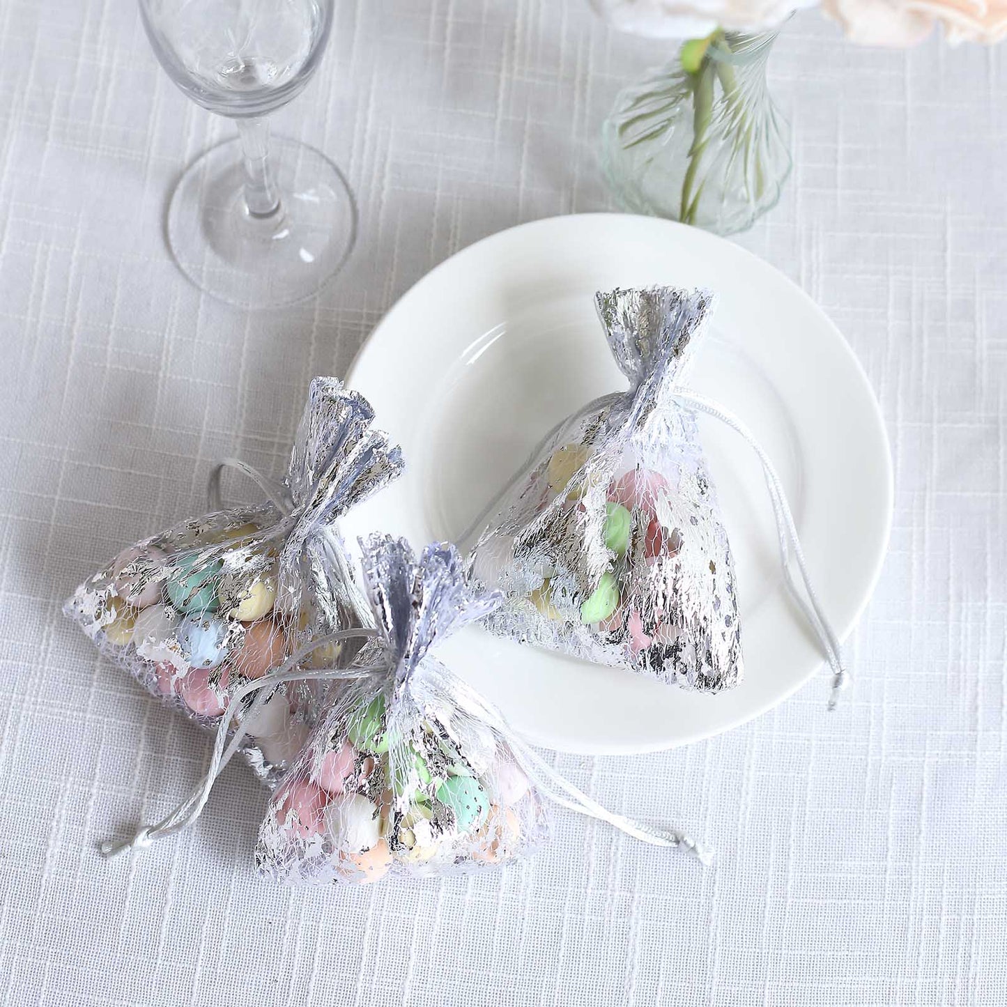 Metallic silver foil drawstring candy bags filled with pastel candies.