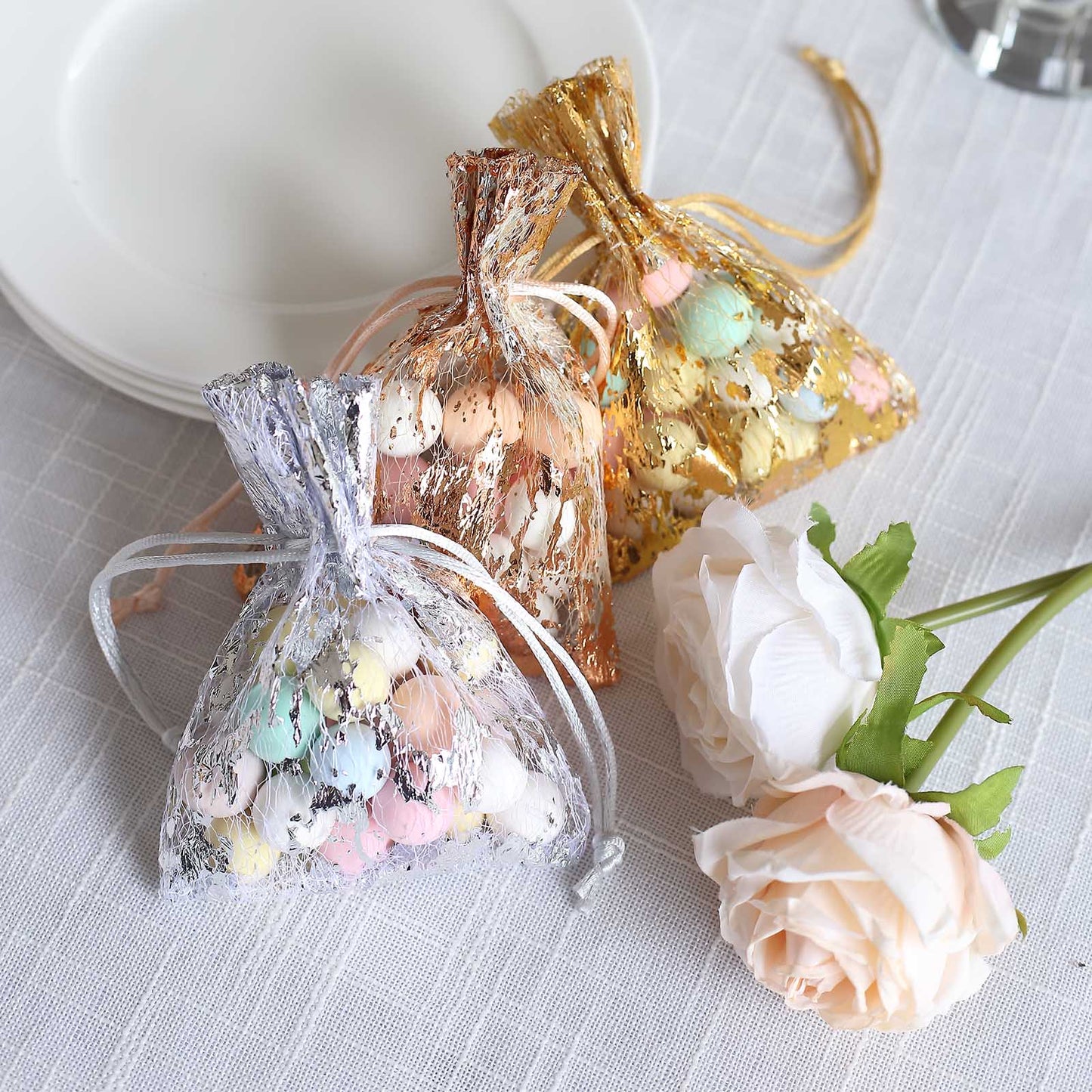 Metallic silver foil drawstring candy bags with pastel candies, wedding party favor.
