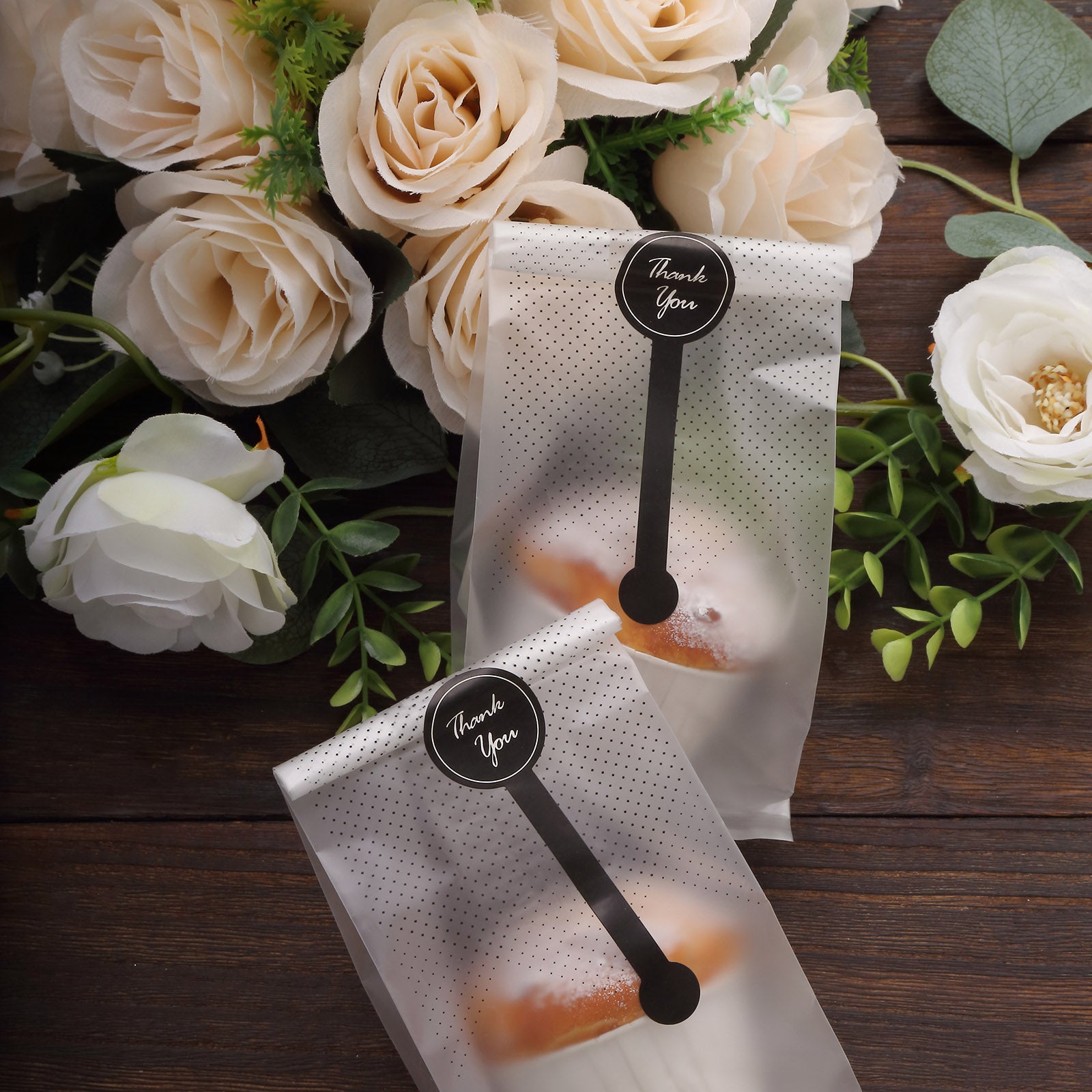 Clear black dotted gift bags with "Thank You" stickers on a wooden surface.
