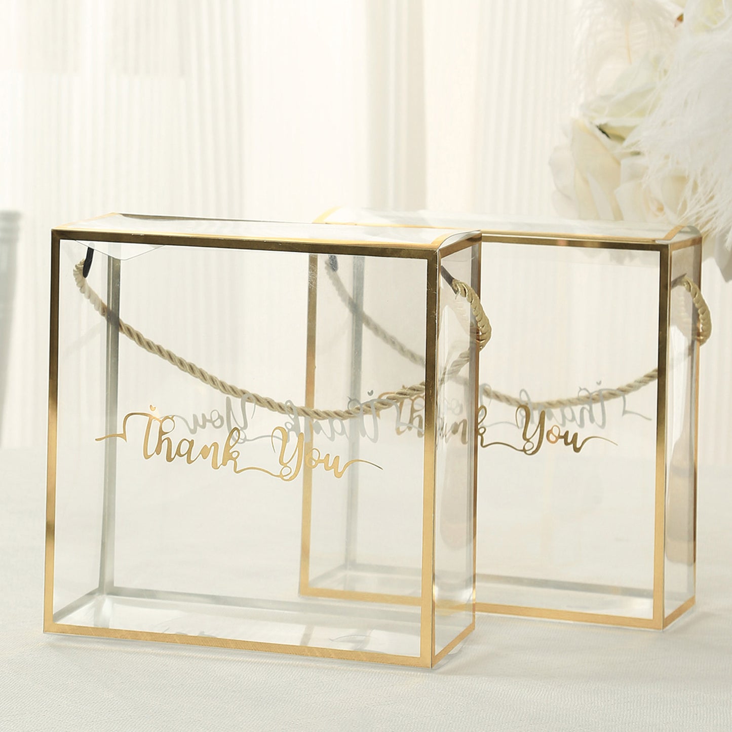 Gold trimmed clear gift boxes with rope handles and "Thank You" print.