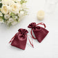 Burgundy satin drawstring favor bags on a white table with flowers.