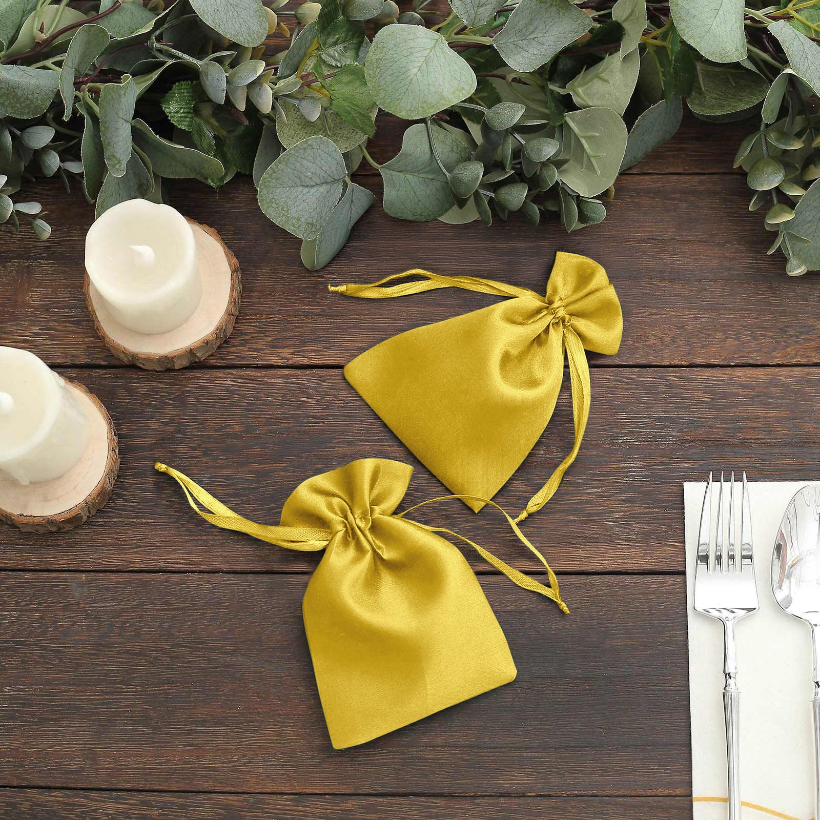 Gold satin drawstring favor bags on a wooden table with greenery.