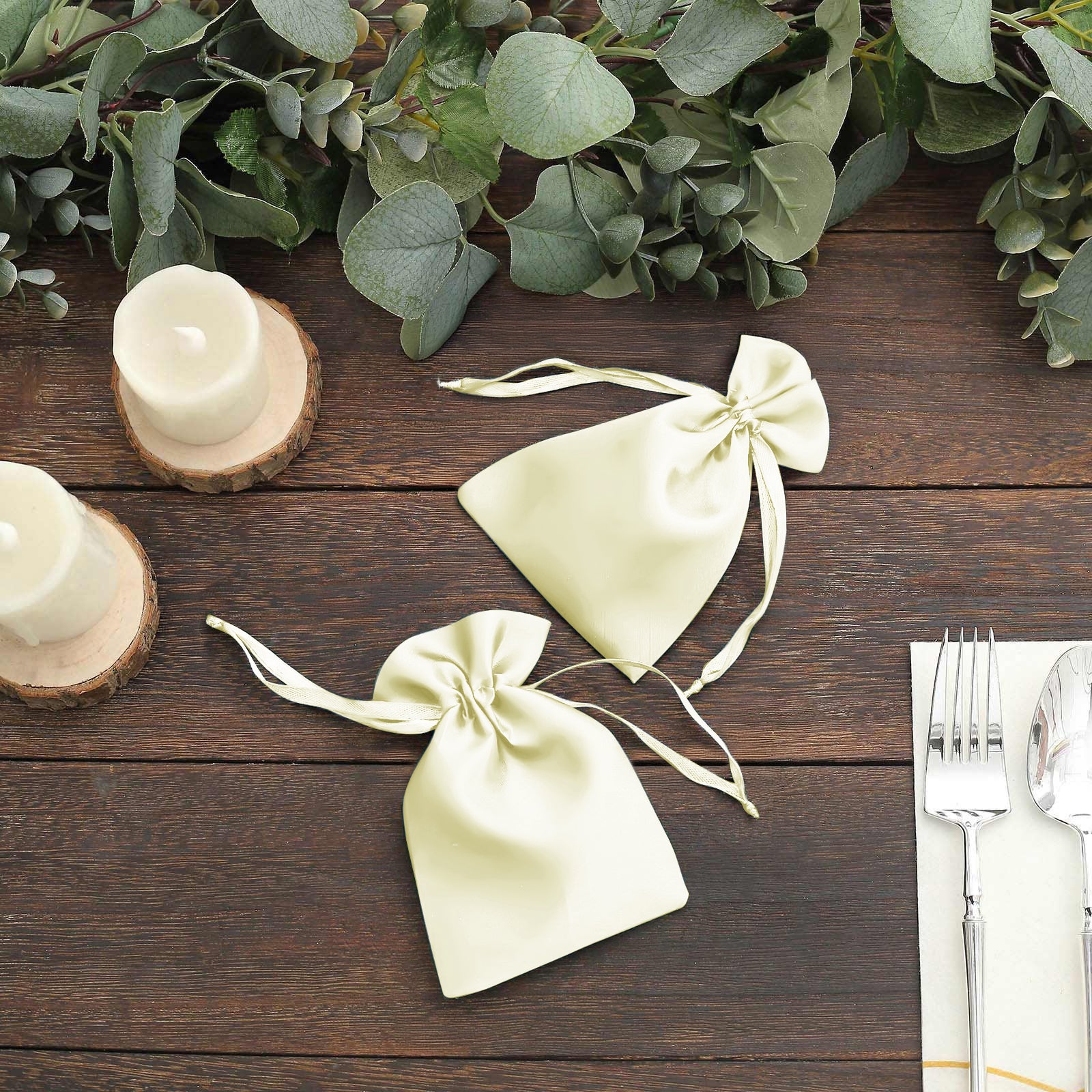 Yellow satin drawstring favor bags on a rustic table with greenery.