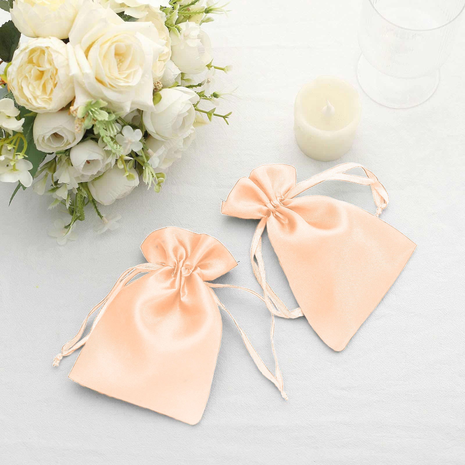 Peach satin wedding party favor drawstring bags on a table.