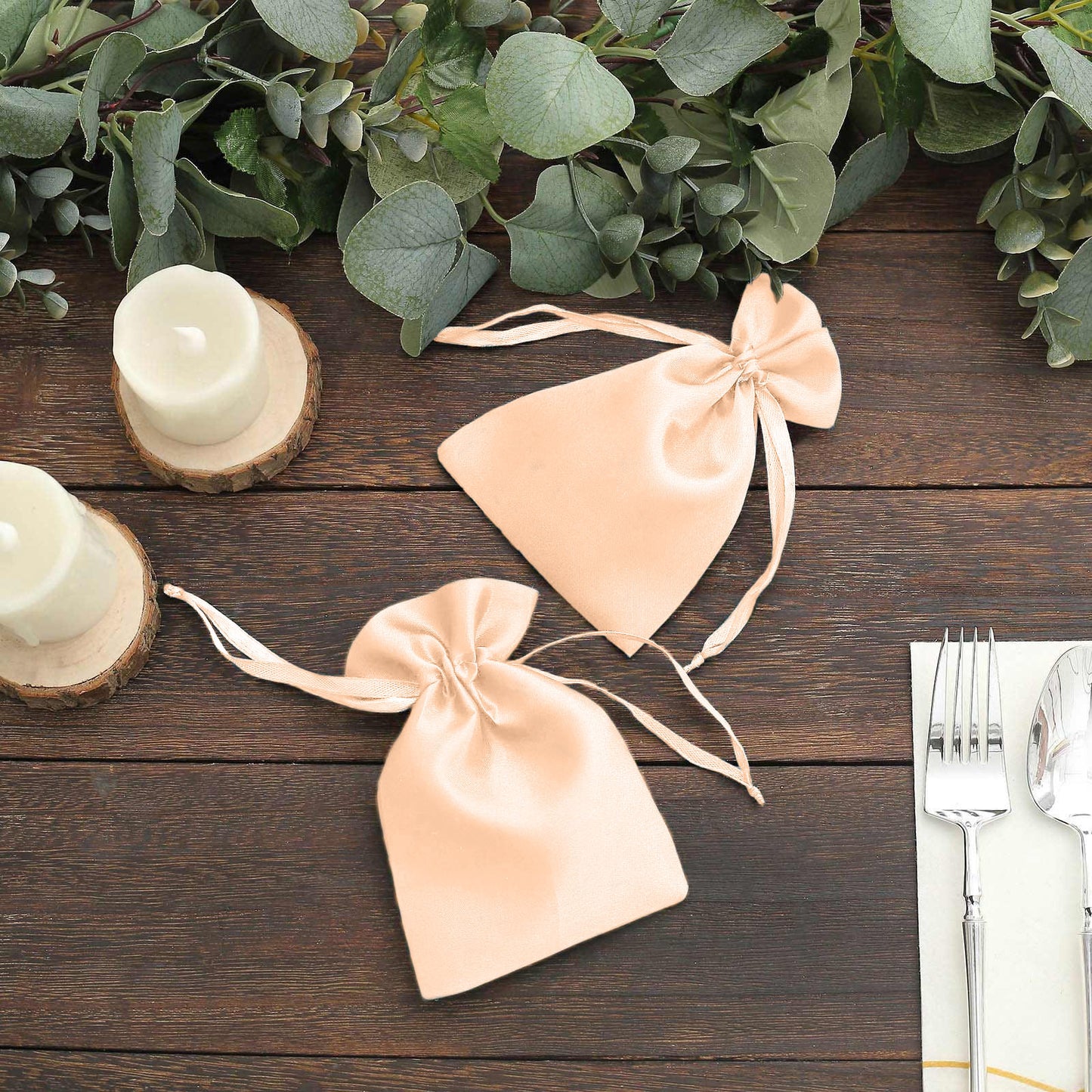 Peach satin drawstring wedding favor bags on a rustic table setting.