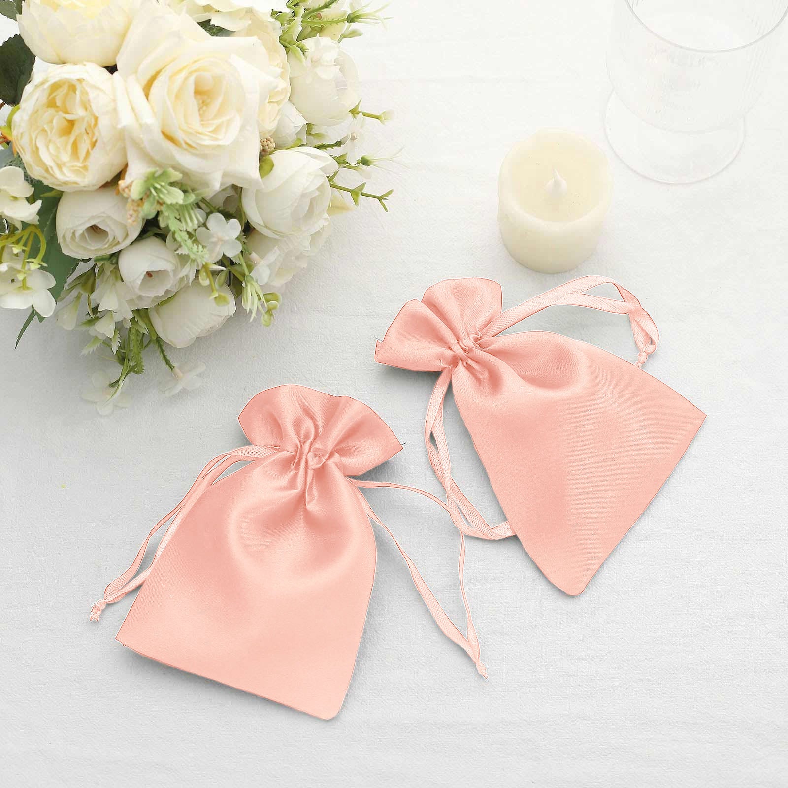 Dusty rose satin drawstring favor bags on a table with flowers.