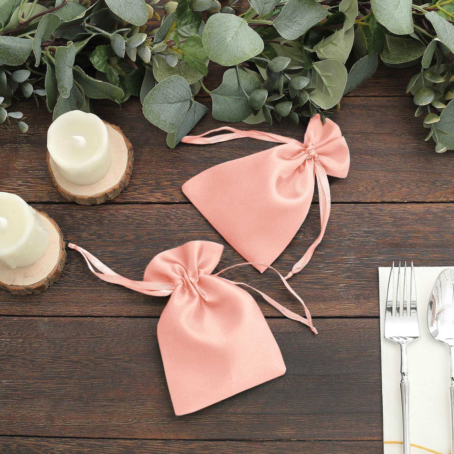 Dusty rose satin drawstring bags on a wooden surface for wedding favors.
