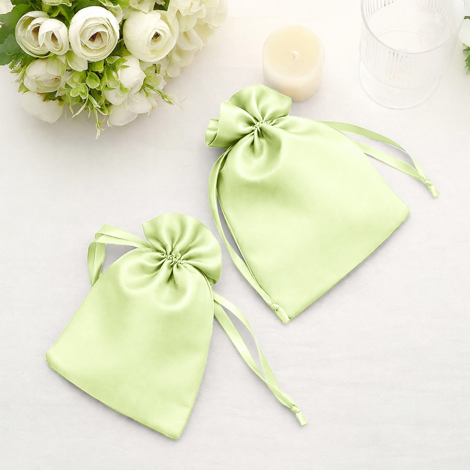 Apple green satin drawstring wedding favor gift bags on a table.