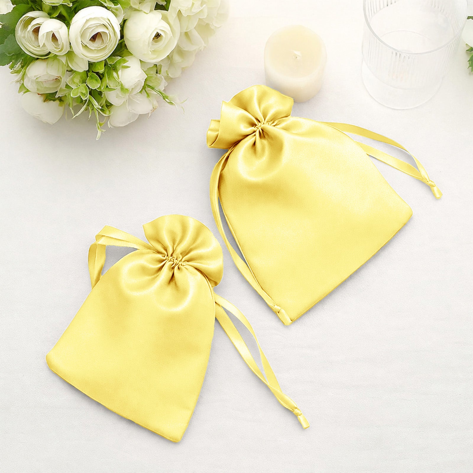 Yellow satin drawstring wedding favor gift bags on a table.