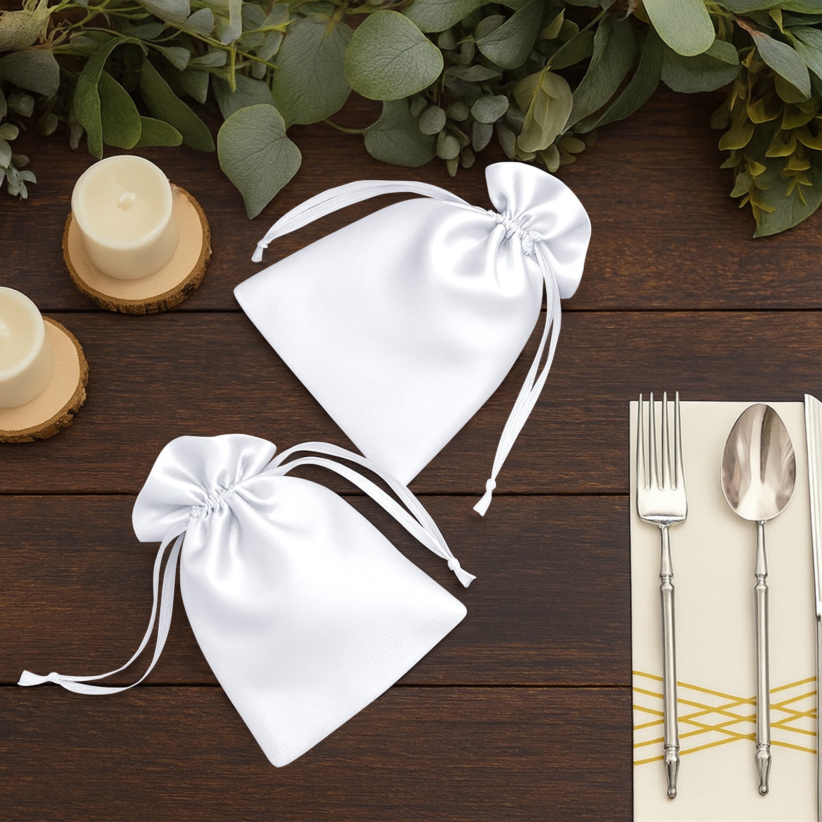 White satin drawstring wedding favor bags on a wooden table.