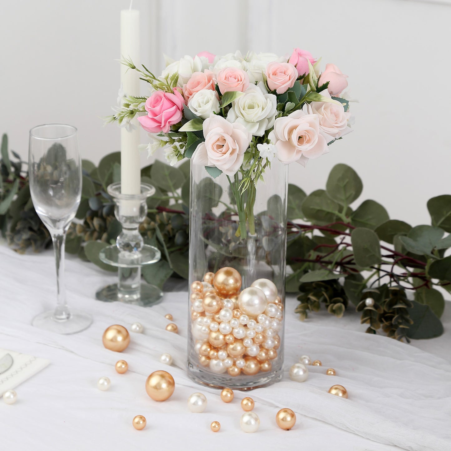 Assorted off white and gold faux pearl beads in a clear vase with flowers.