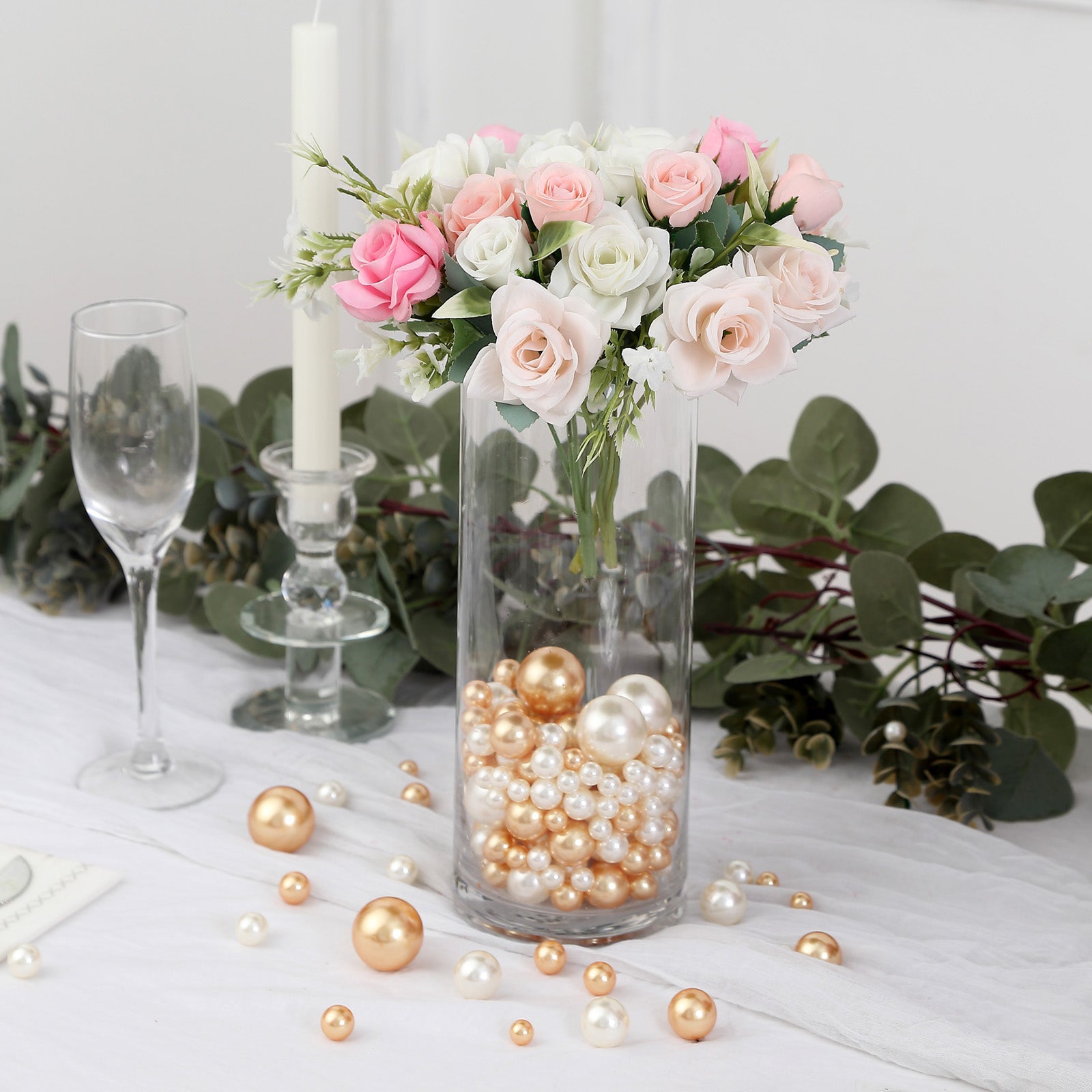 Assorted off white and gold faux pearl beads in a clear vase with flowers.