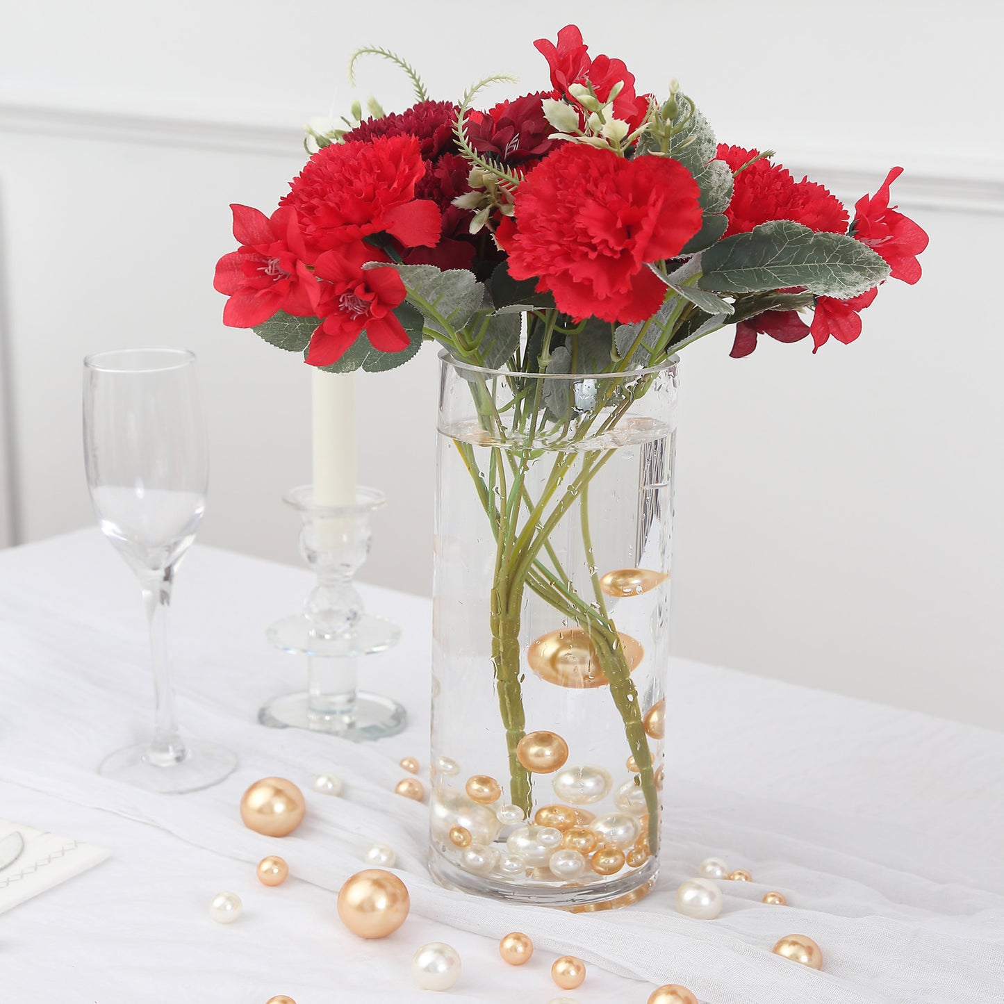 Assorted off white and gold faux pearl beads in a glass vase with flowers.