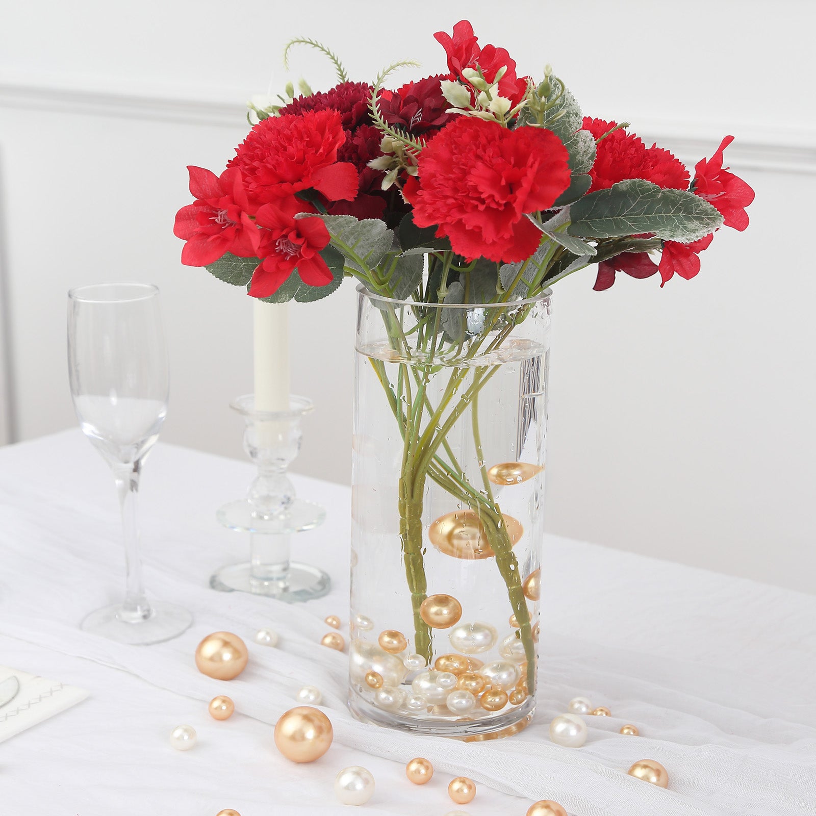 Assorted off white and gold faux pearl beads in a glass vase with flowers.
