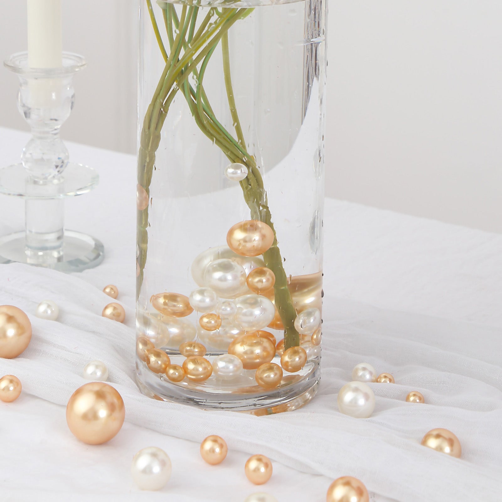 Assorted off white and gold faux pearl beads in a clear vase.