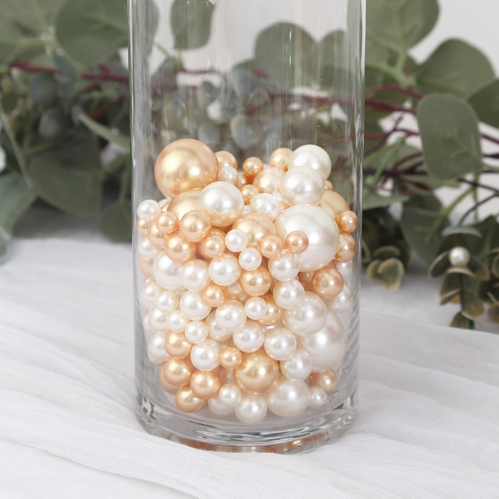 Assorted off white and gold faux pearl beads in a glass vase.