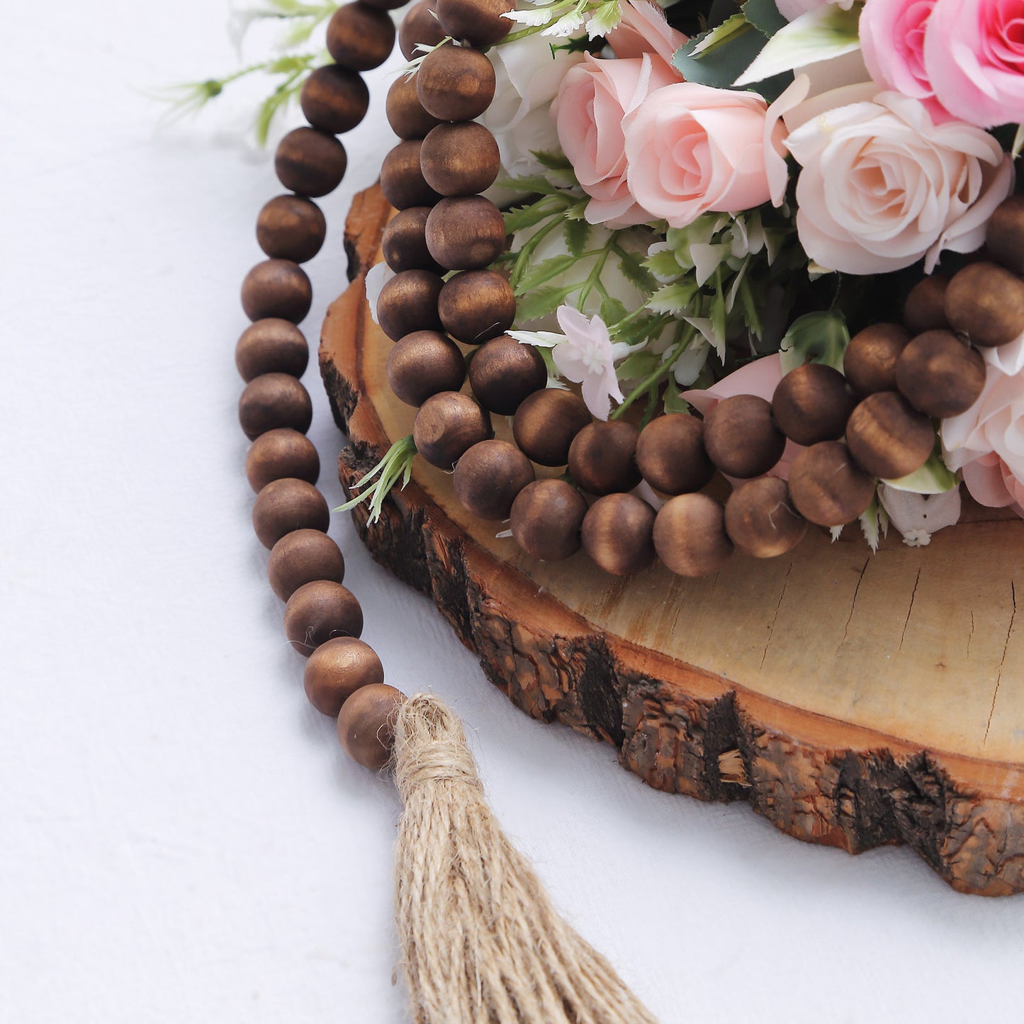 Brown rustic wood bead garland with tassels on a wooden surface.