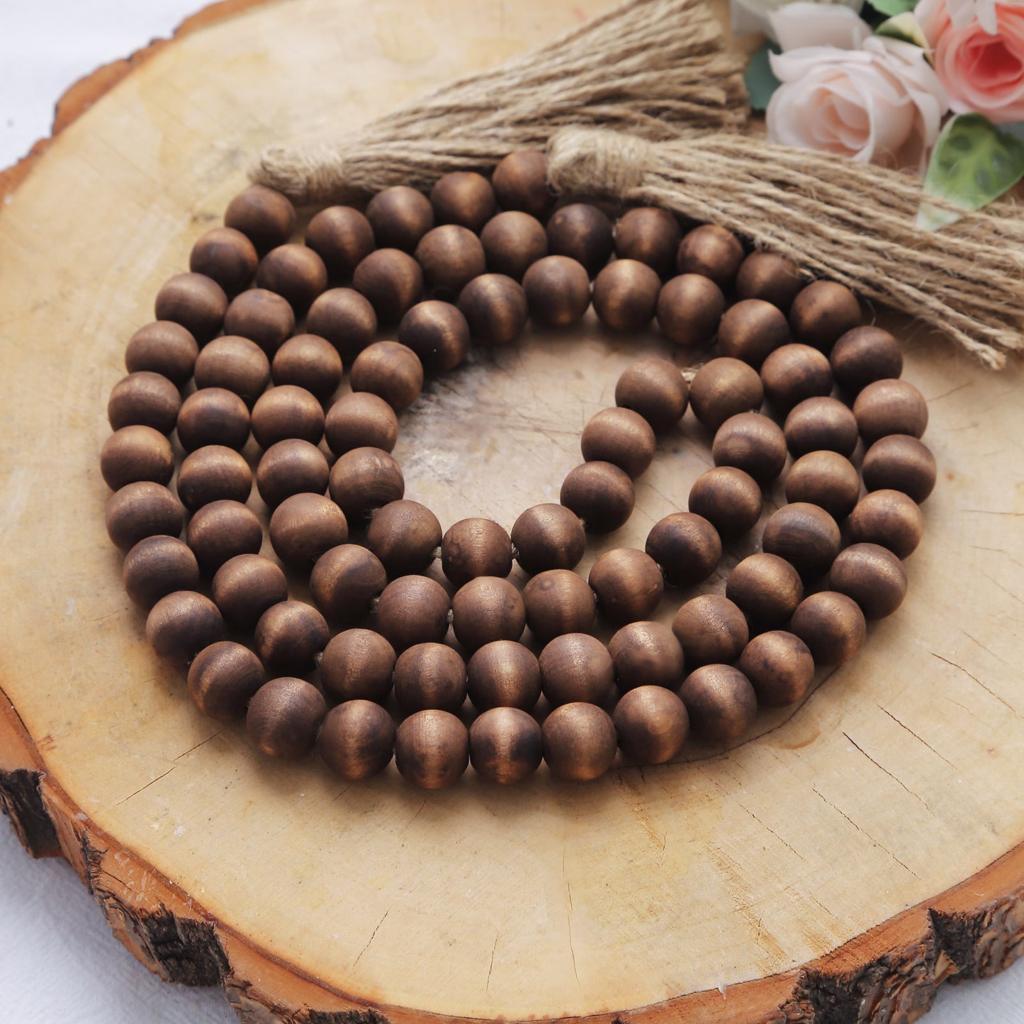Brown rustic wood bead garland with tassels on a wooden surface.