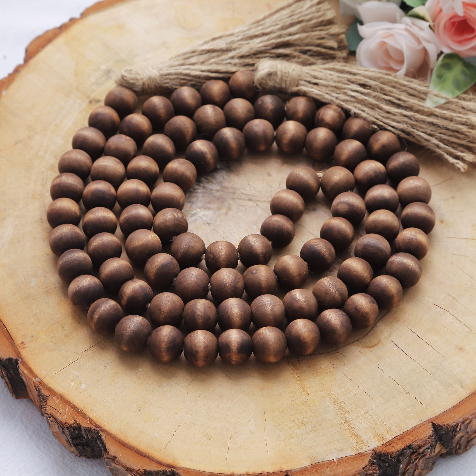 Brown rustic wood bead garland with tassels on a wooden surface.