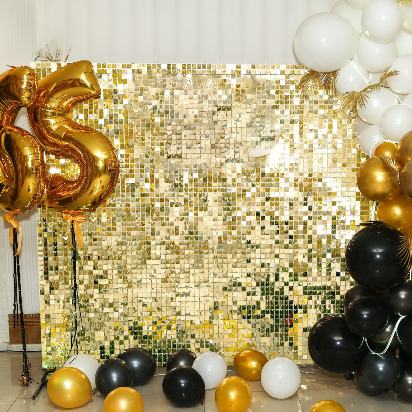 Shiny gold sequin shimmer wall backdrop with black and gold balloons.