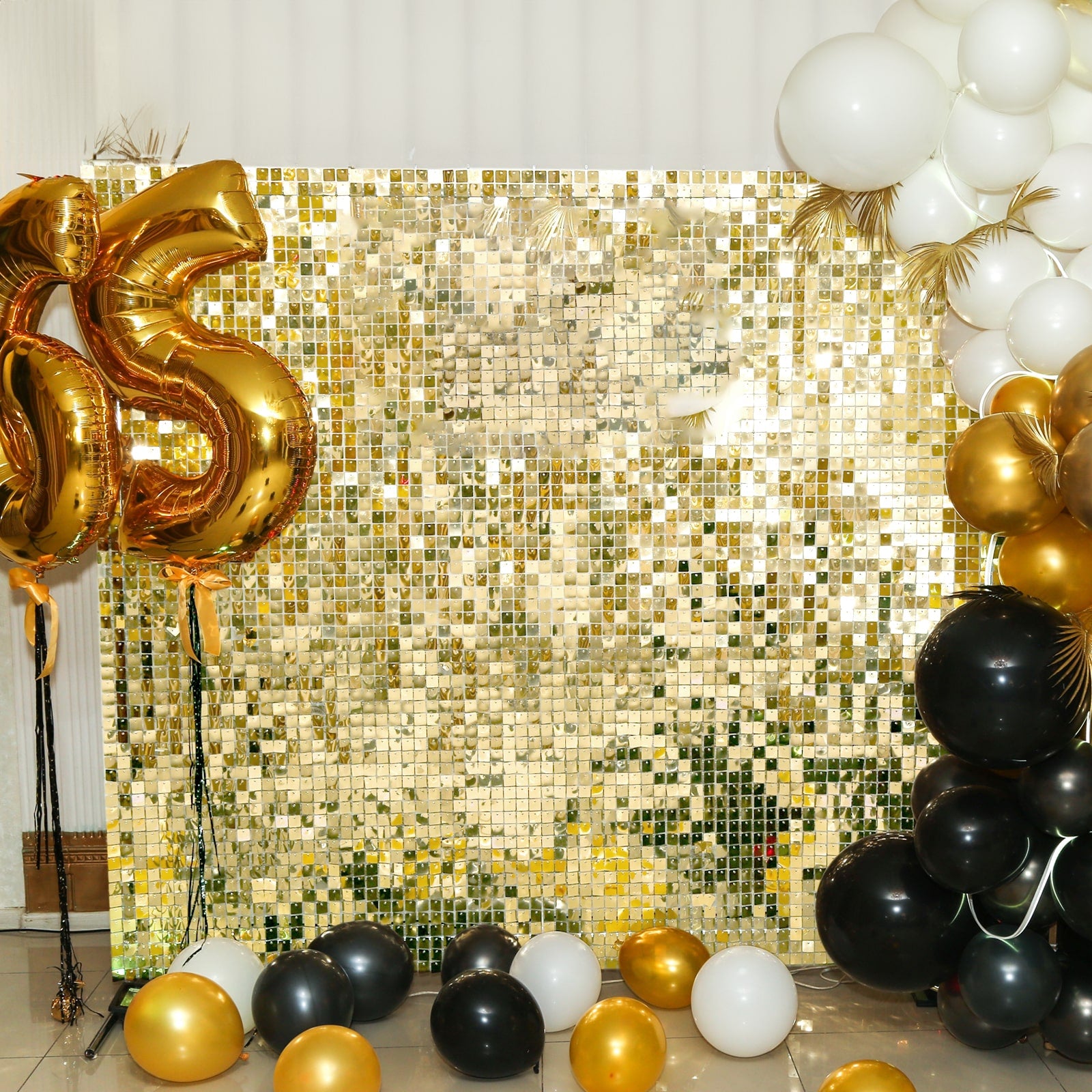 Shiny gold sequin shimmer wall backdrop with black and gold balloons.