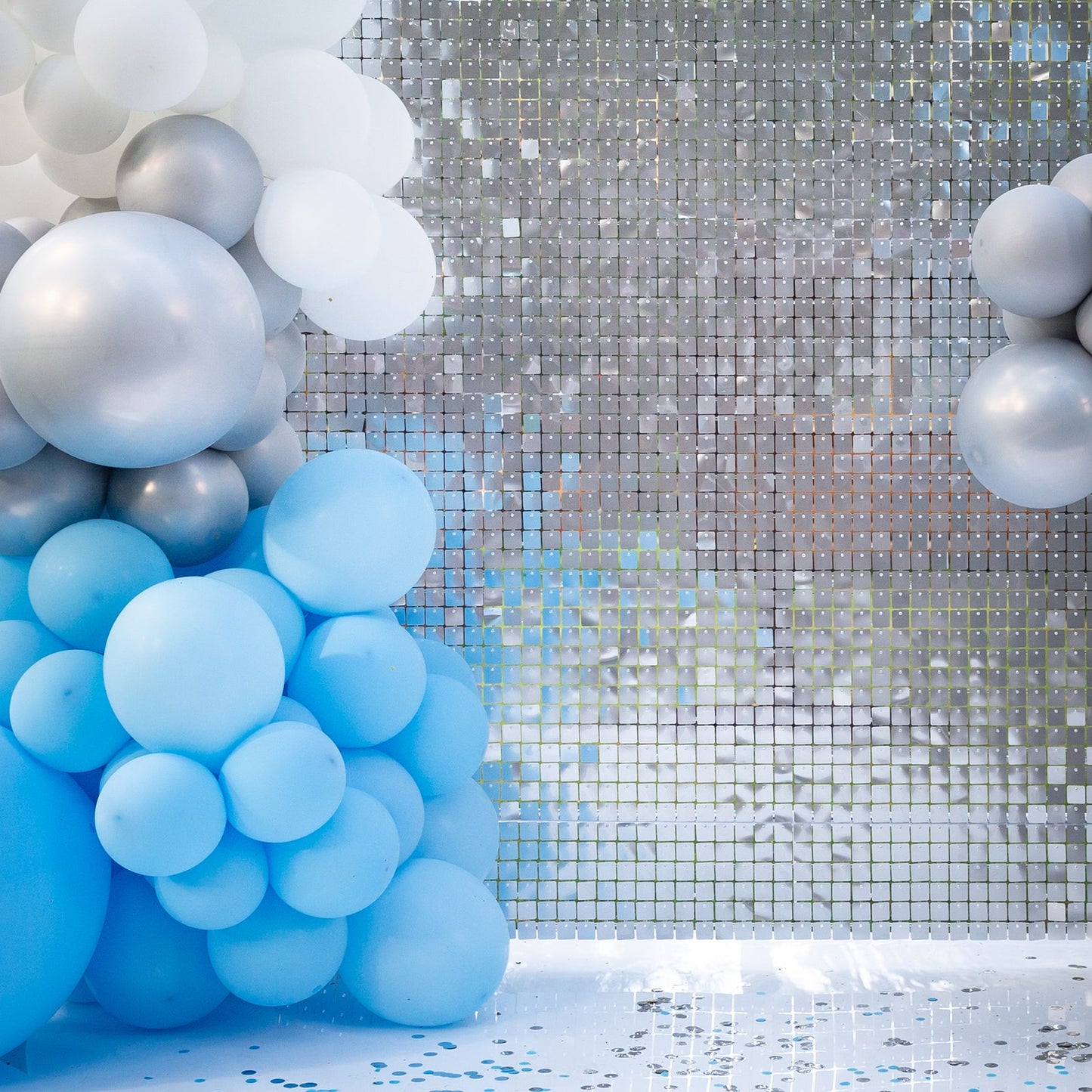 Shiny silver sequin wall backdrop with blue balloon decorations.