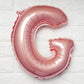 Rose gold letter balloon "G" against a white textured background.