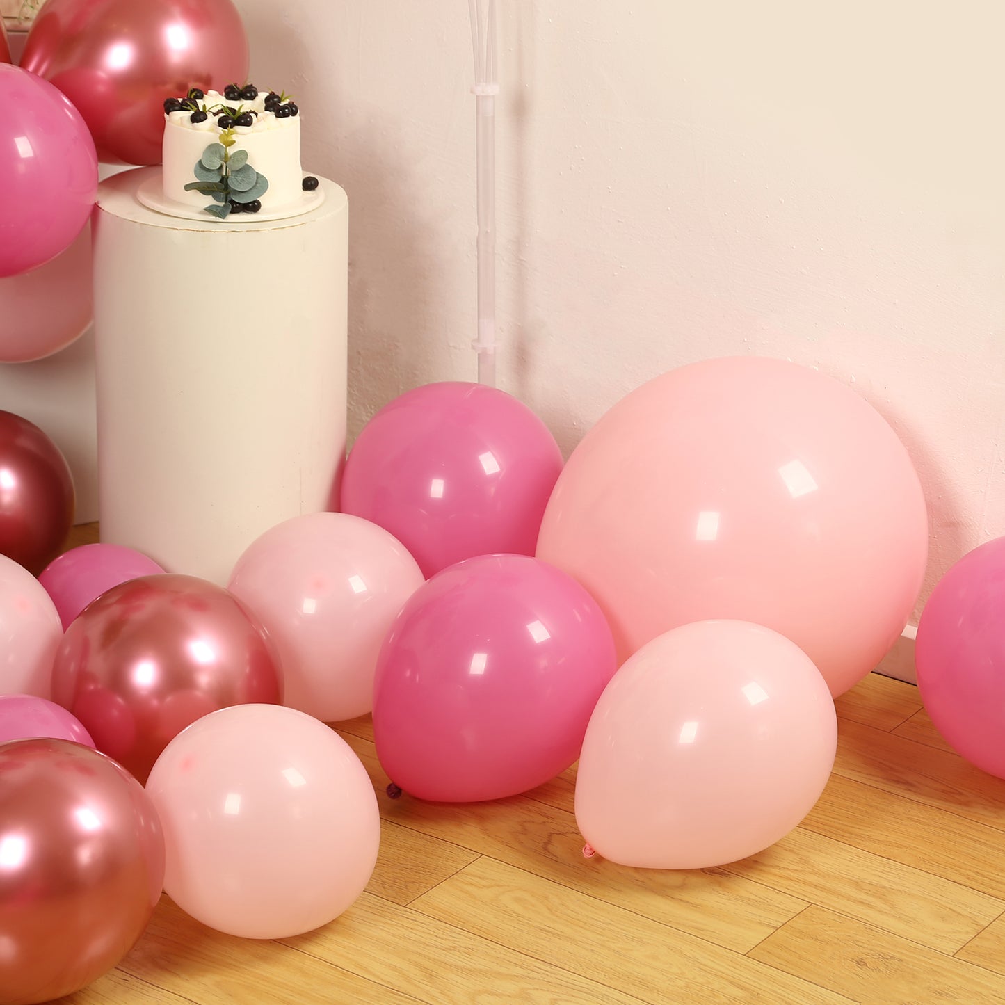 Rose gold pink biodegradable balloon arch kit on wooden floor.