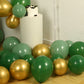 Gold and green biodegradable balloon arch kit on a floor with a cake.