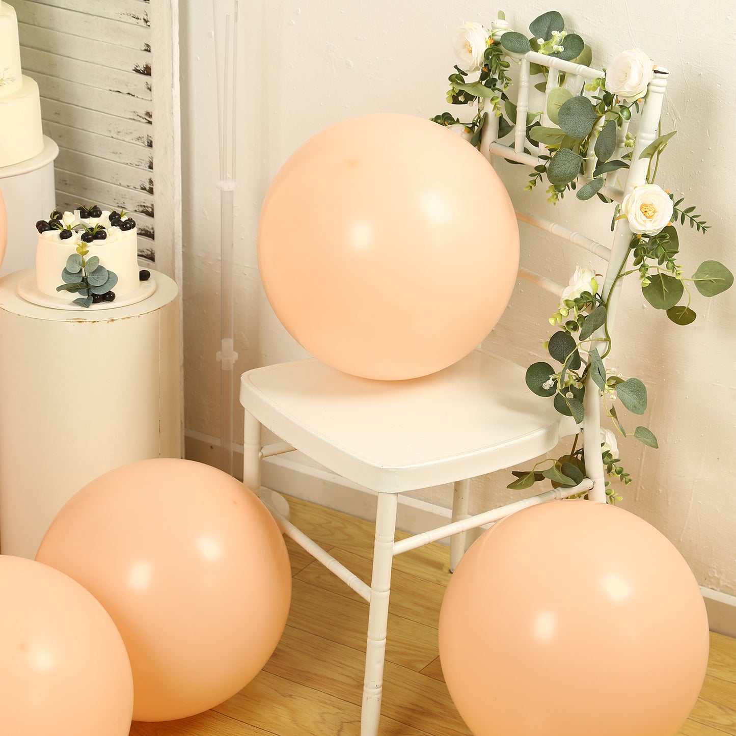 Matte pastel blush biodegradable balloons on a white chair with greenery.