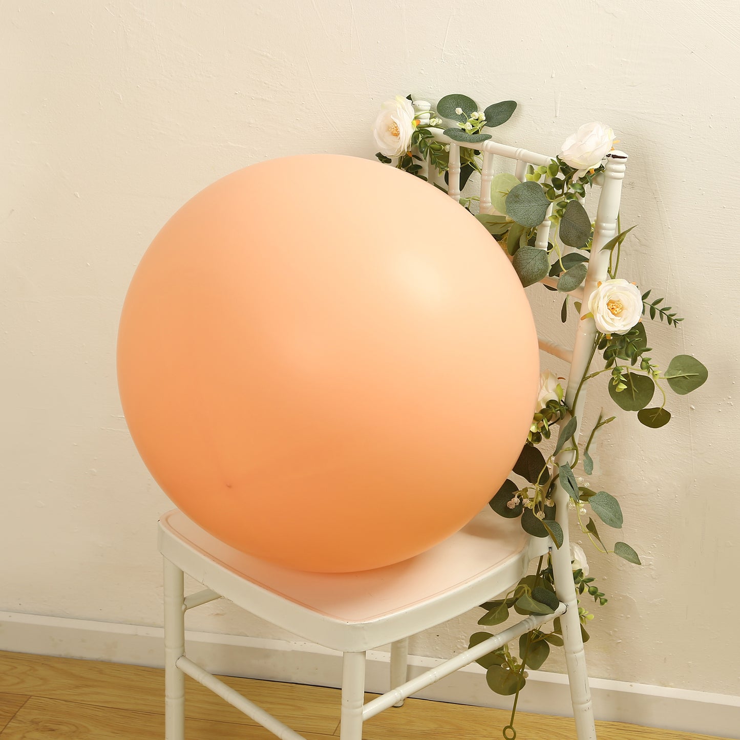 Large matte pastel blush biodegradable balloon on a chair amidst greenery.