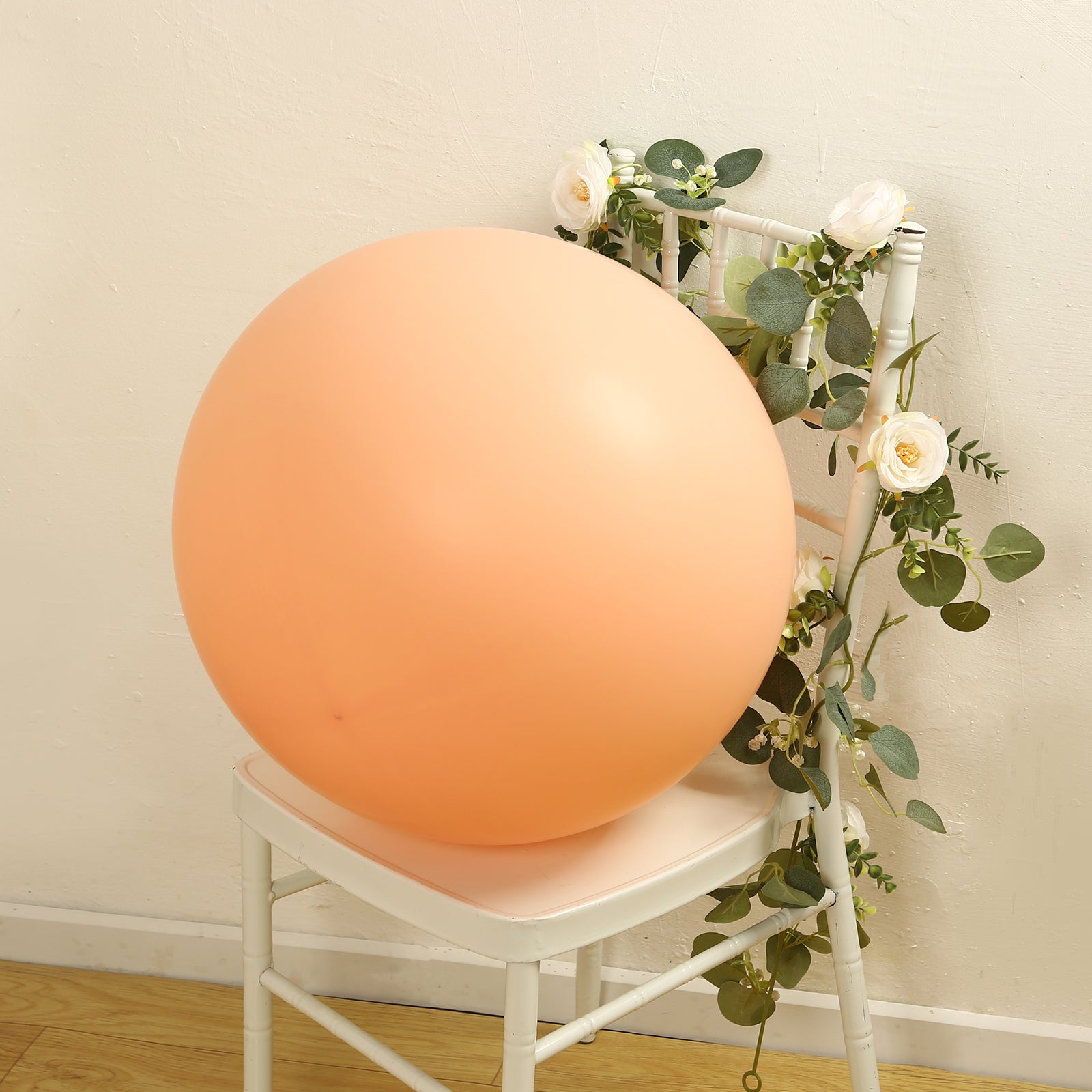 Large matte pastel blush biodegradable balloon on a chair amidst greenery.