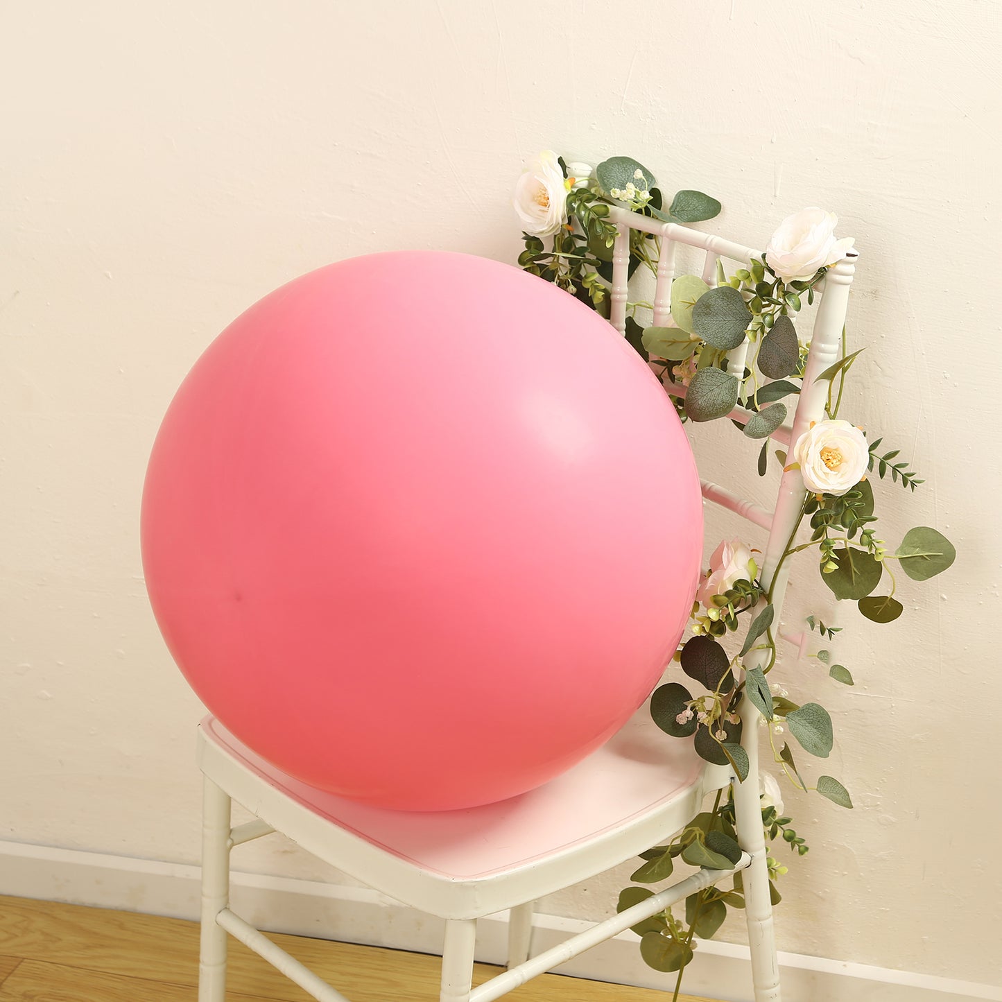 Large matte pastel pink biodegradable balloon on a chair with greenery.