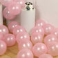 Blush biodegradable balloons scattered around a cake on a white pedestal.