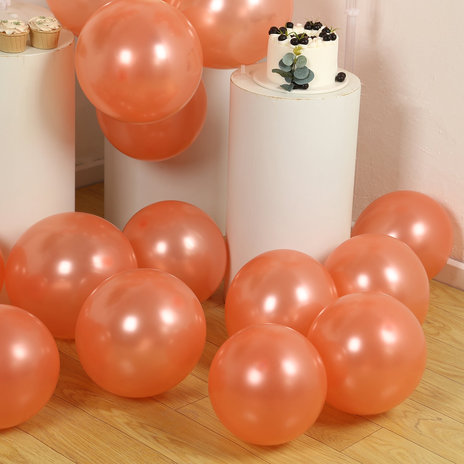 Rose gold biodegradable balloons scattered on a wooden floor.