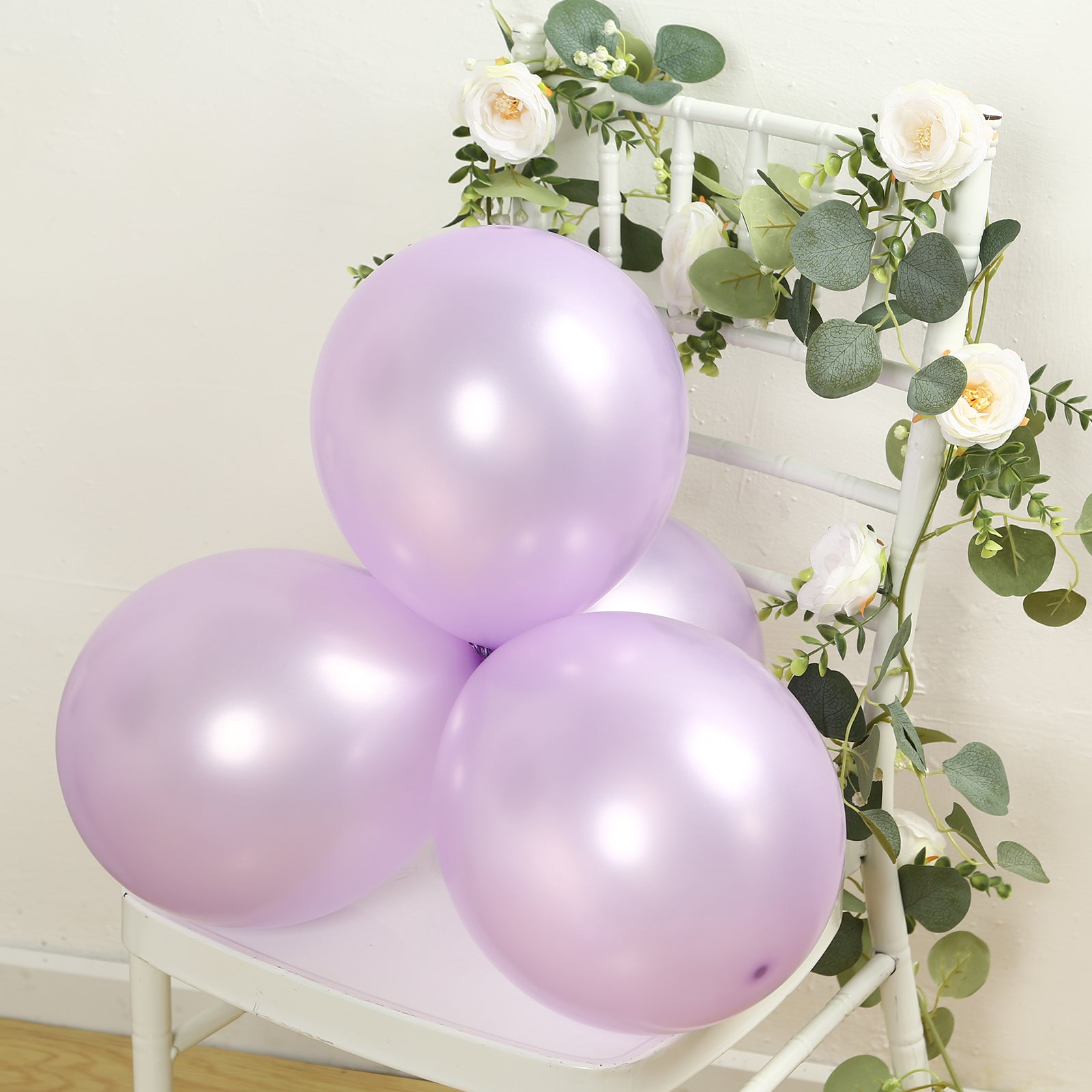 Lavender lilac biodegradable balloons on a chair with greenery and flowers.