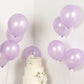 Lavender biodegradable balloons beside a white cake with flowers.