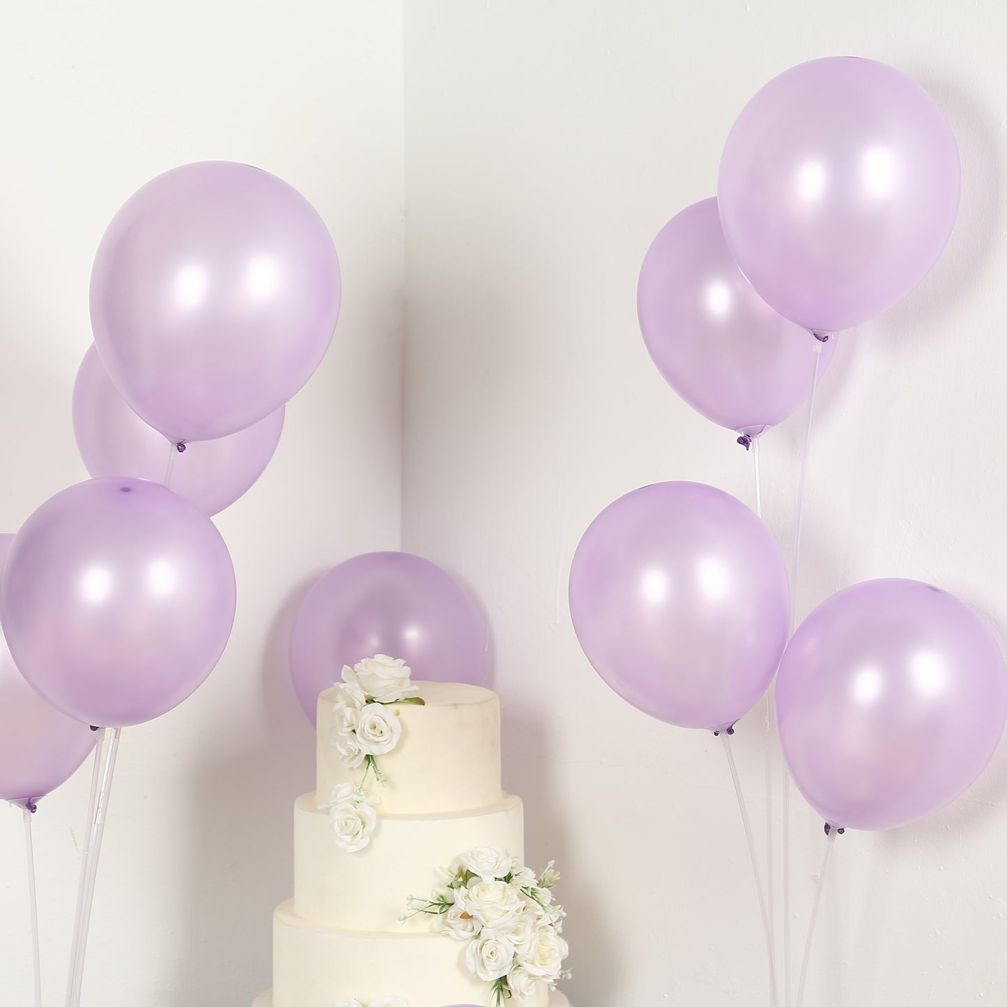 Lavender biodegradable balloons beside a white cake with flowers.