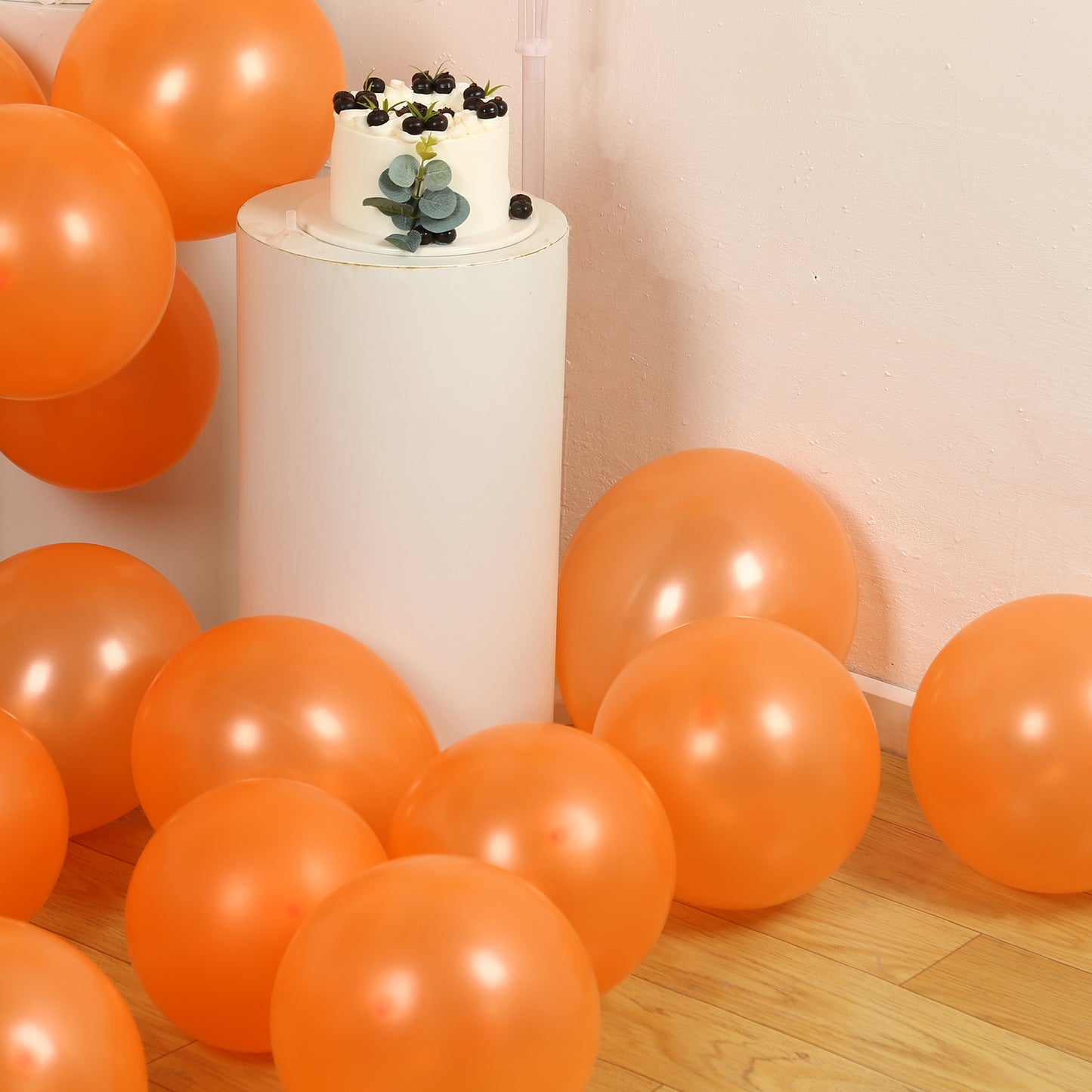 Orange biodegradable balloons scattered around a cake on a white pedestal.