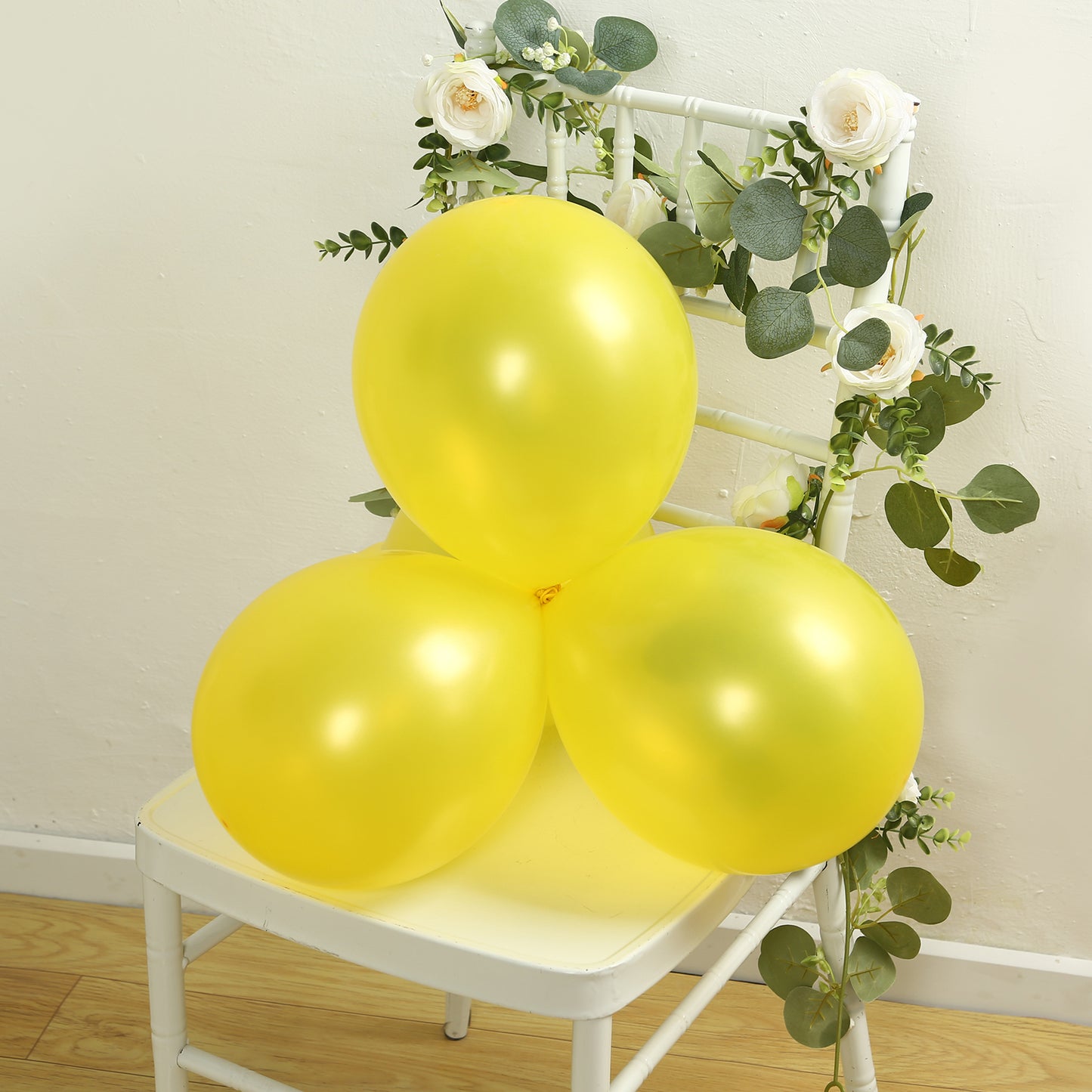 Yellow biodegradable balloons on a chair with greenery and flowers.
