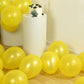 Yellow biodegradable balloons scattered near a cake on a white pedestal.