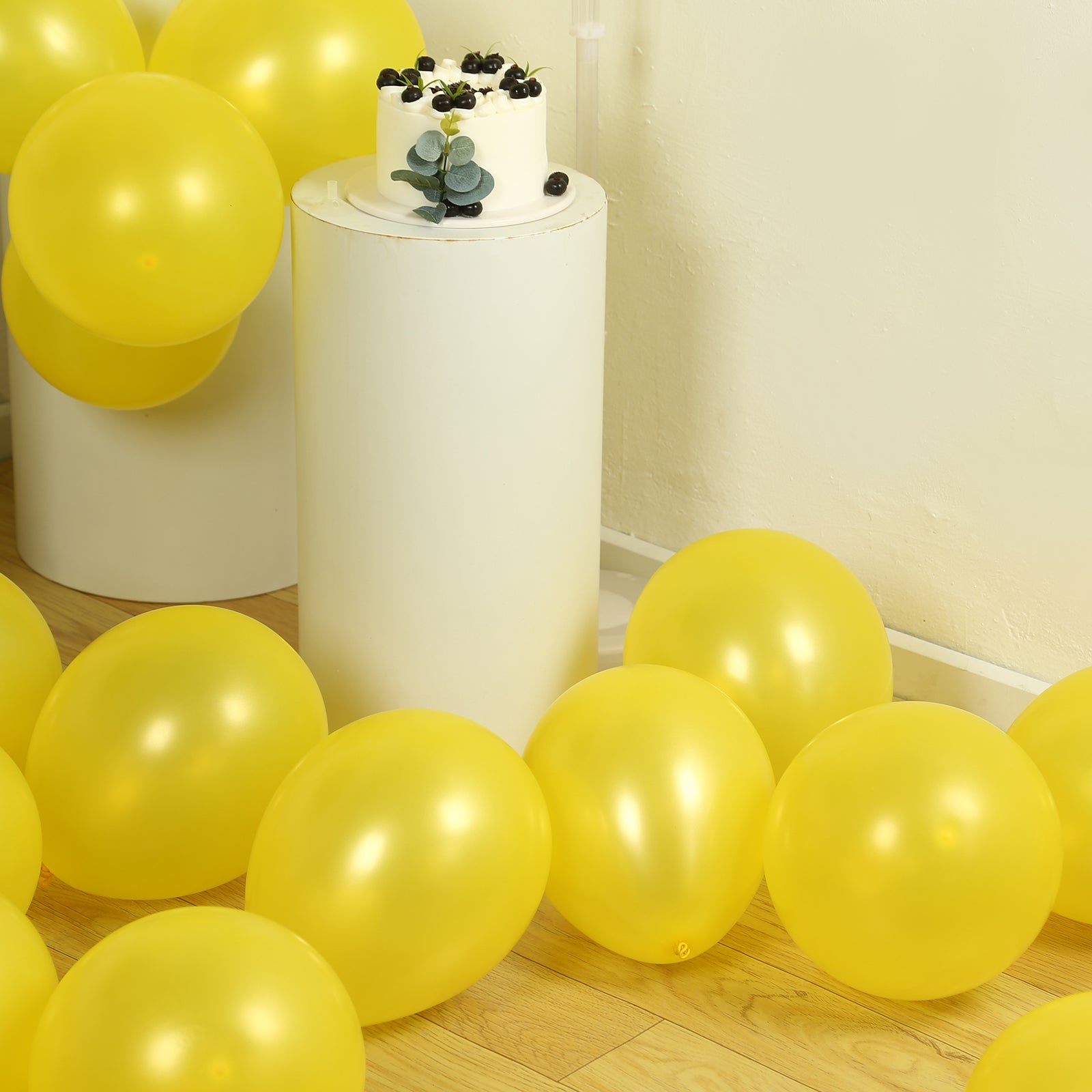 Yellow biodegradable balloons scattered near a cake on a white pedestal.