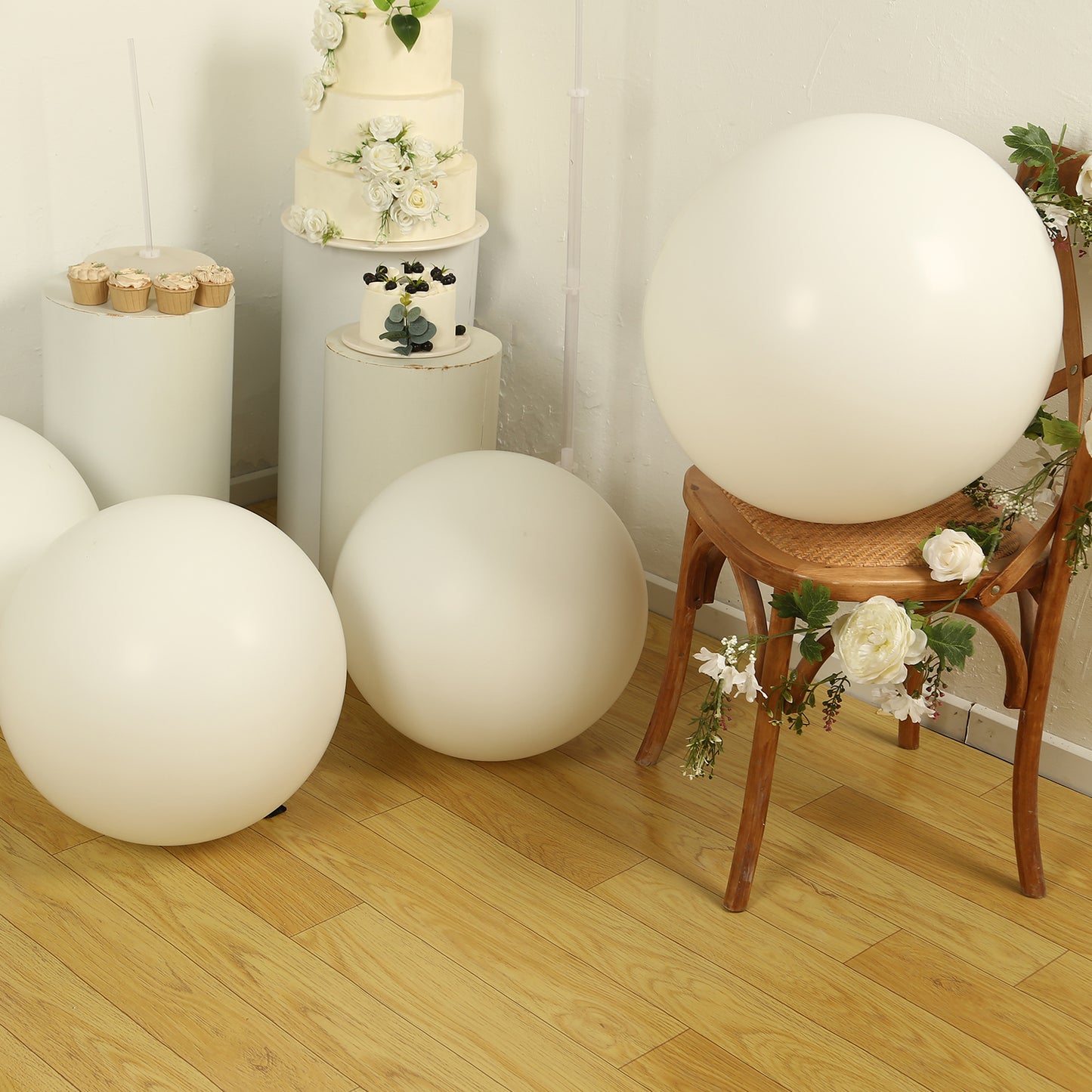 Large off white biodegradable balloons on a wooden floor with floral decor.