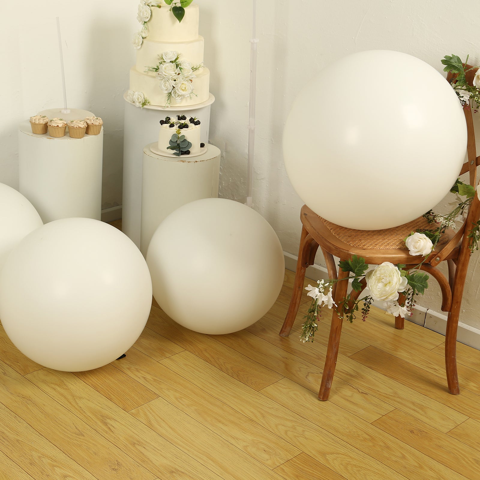 Large off white biodegradable balloons on a wooden floor with floral decor.