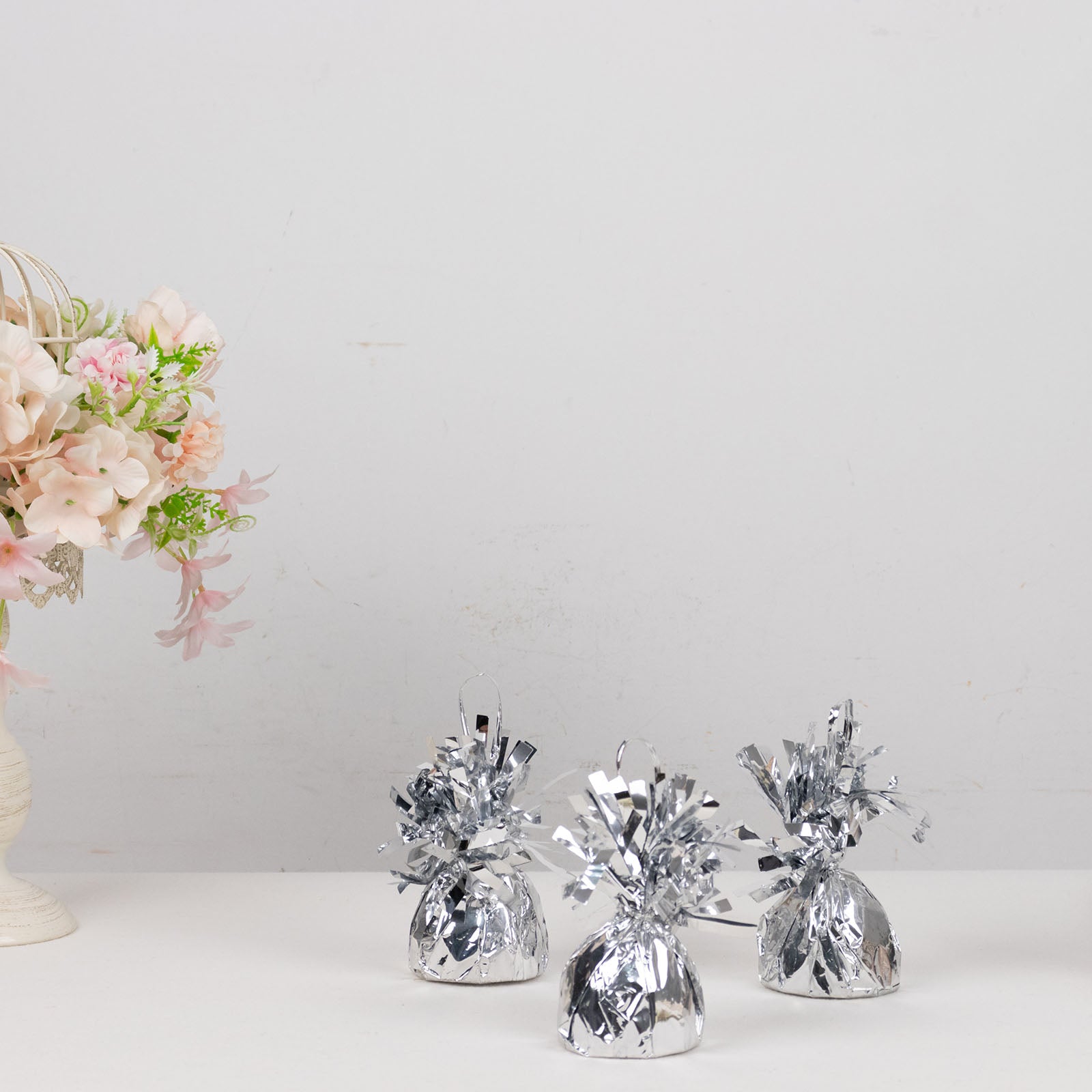 Metallic silver foil tassel top party balloon weights on a table.