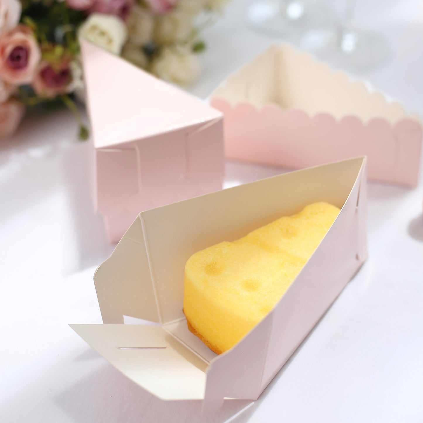 Blush triangular cake slice boxes with scalloped tops and yellow dessert inside.