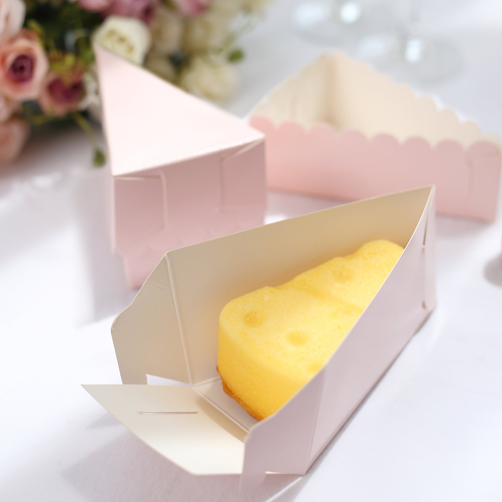 Blush triangular cake slice boxes with scalloped tops and yellow dessert inside.