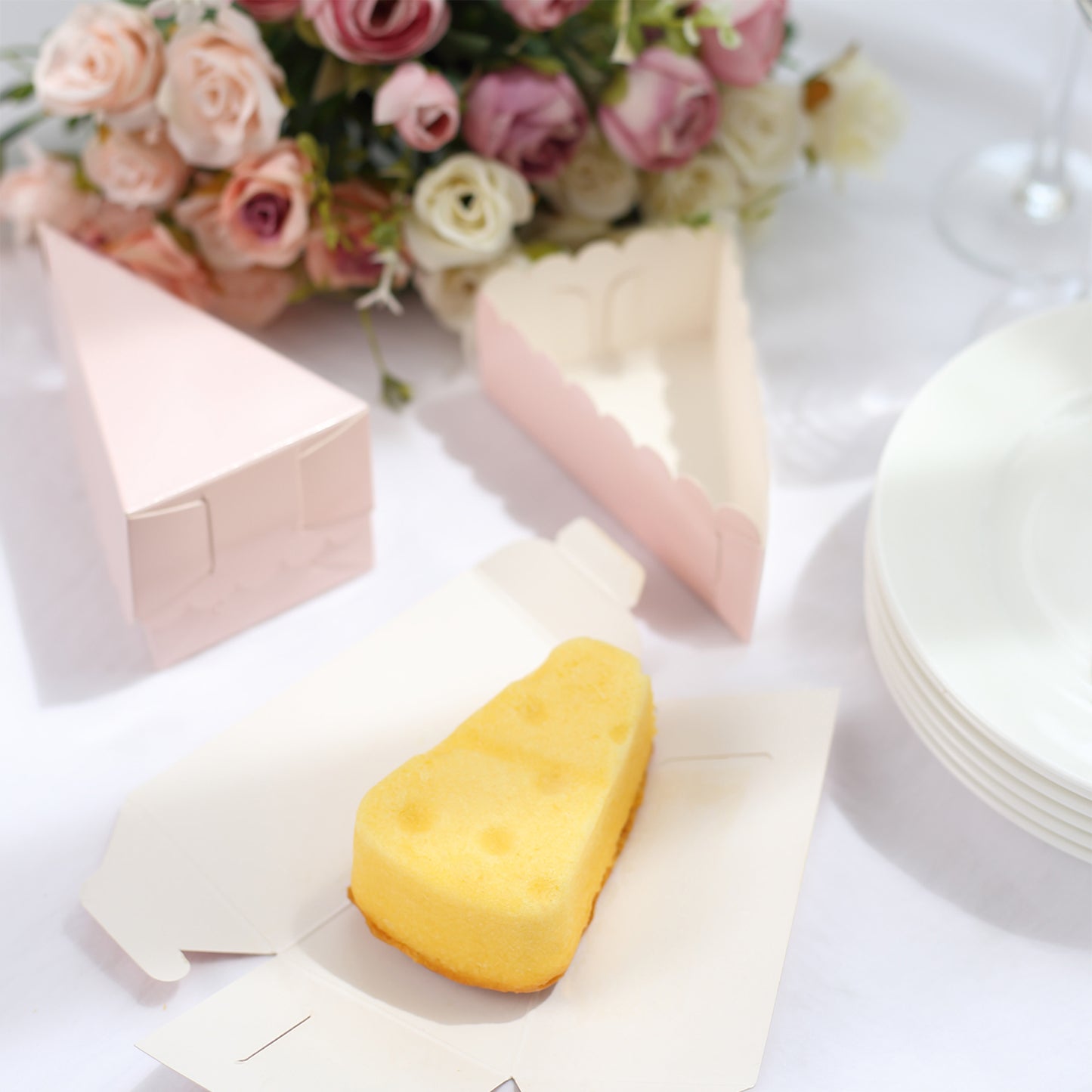 Blush triangular paper cake box with dessert slice on a table setting.